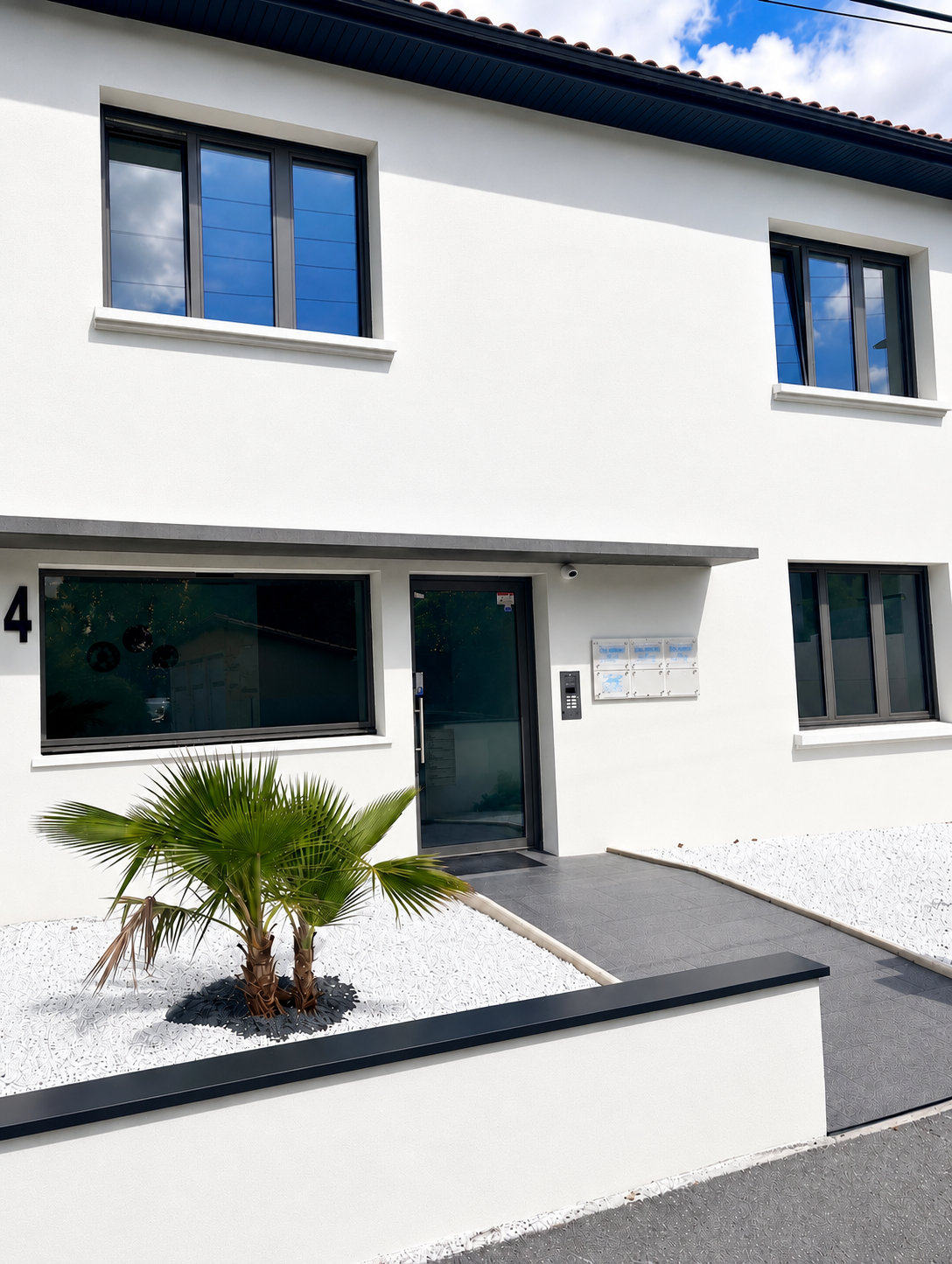 Façade extérieure d’un bâtiment blanc avec entrée vitrée et palmier